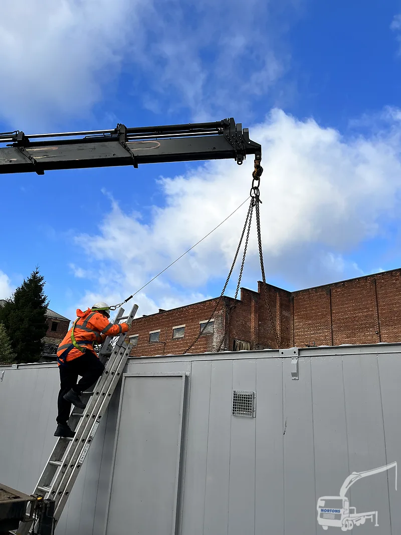 Hiab crane lorry lifting a cabin against a clear sky — Nortons Hiab Services