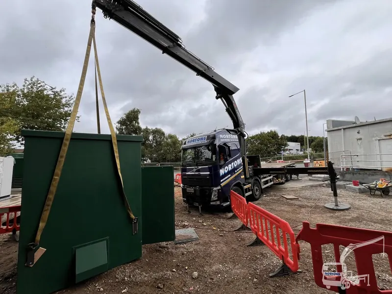 Lorry crane lifting a green security cabin into place