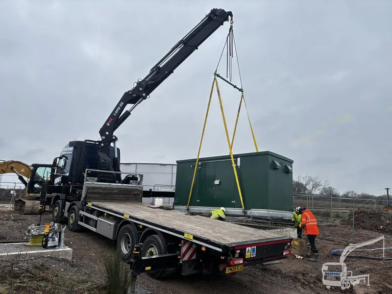 Hiab lorry lifting a green cabin onto prepared ground