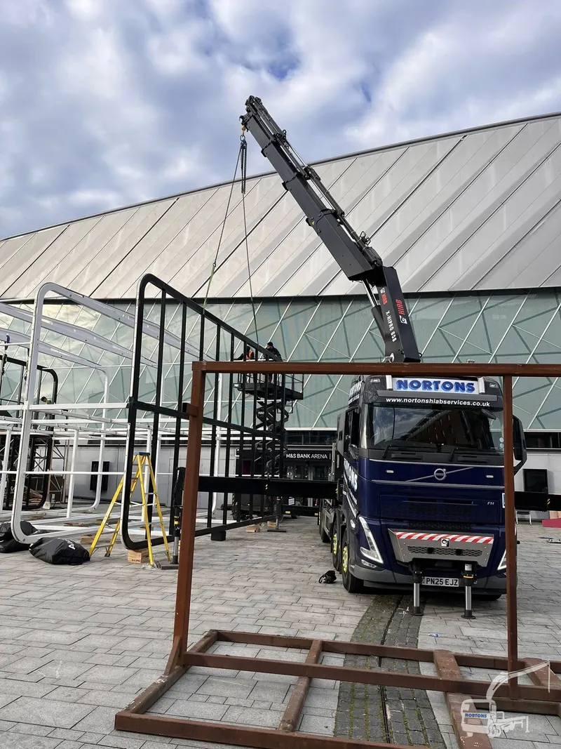 Truck mounted crane lifting a steel frame against a blue sky